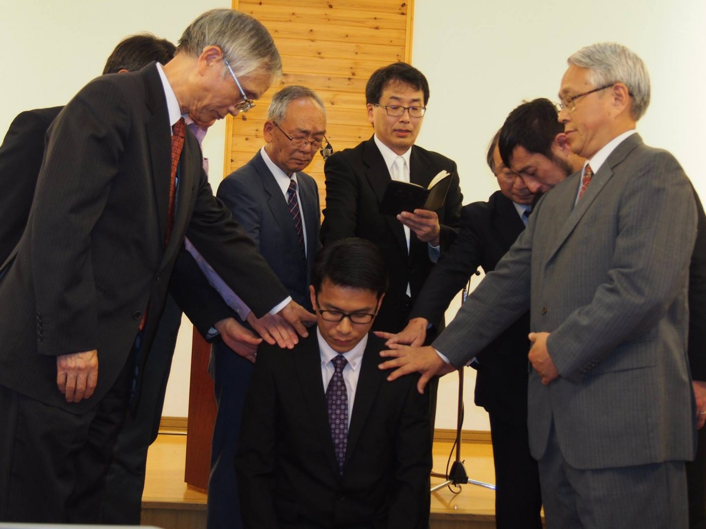 Pastor Tak (kneeling) being installed as the senior pastor of Sapporo Minami Evangelical Christ Church in October 2015, with Pastor Yasuji Honda (standing, second from left).