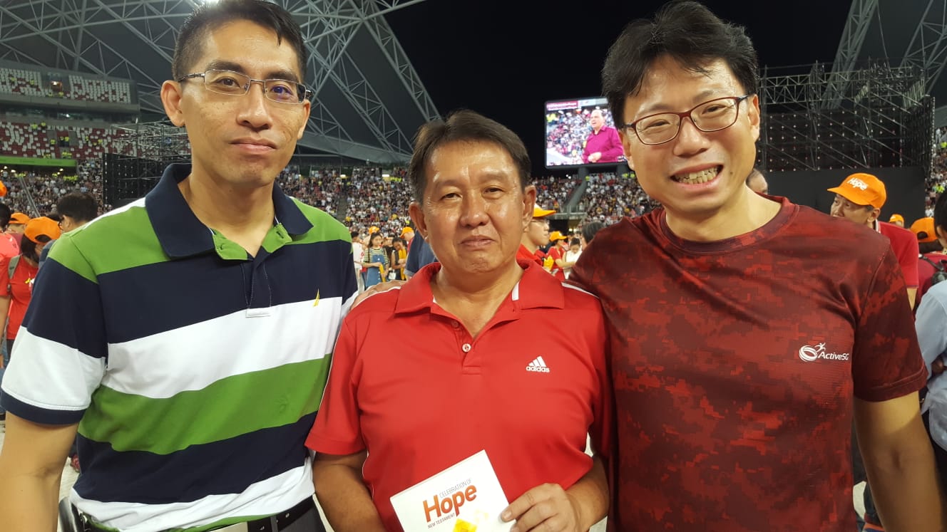 Yap Hui Kheng (middle) received Christ at the rally after his colleague, Lim Hong Khiang (right), took a step of faith to invite him. Photo by Karen Tan.