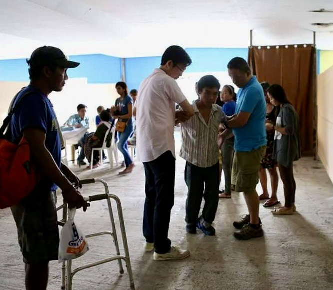 Clarence's experience in the hospital changed the way he prays for healing for the sick.  He is pictured here (in white) praying for a disabled man while on a mission trip to the Philippines.
