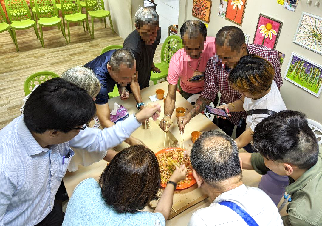 A group of seven homeless people and three social workers and volunteers celebrated the Lunar New Year on January 29, 2020 by tossing a <i>yu sheng</i> at the Homeless Night Cafe run by Presbyterian Community Services and Homeless Hearts of Singapore. Faces have been blurred out to protect their identity. Photo by Gracia Lee.