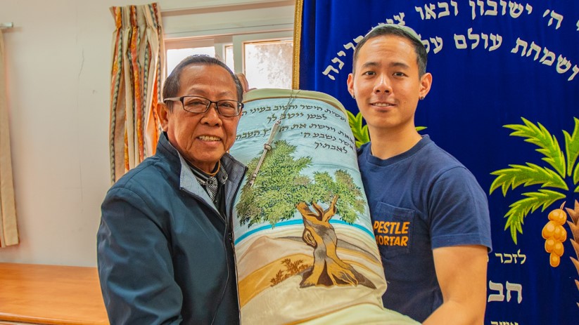 Tan with his father at a Messianic Jewish community in Israel called a moshav. They are holding Torah that is used in the community.