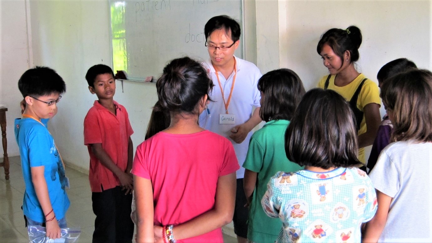 Ethan (far left) and Gerald (centre in white) on mission trip to Cambodia talking to the local children in a school. Ethan was the first of the Tan children to follow his father into Cambodia before the whole family went in 2014.