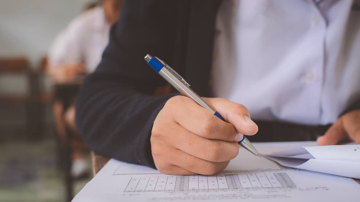 Close up hand of students reading and taking exam sheets exercises answer with stress in classroom