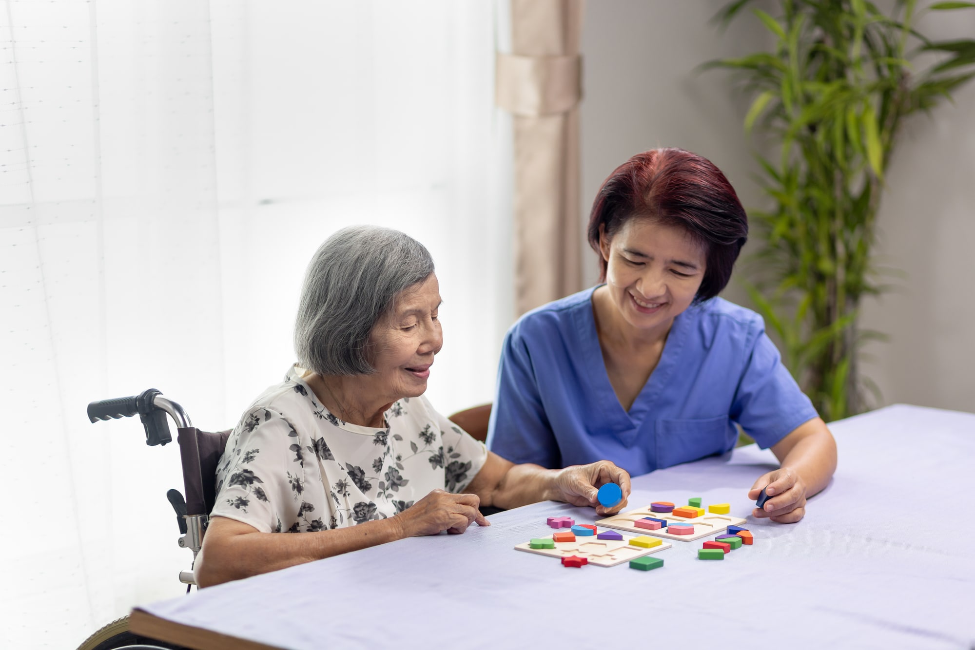 Caregiver and senior woman playing wooden shape puzzles game for